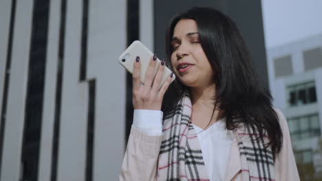 mujer de negocios grave grabando mensaje de voz en el teléfono inteligente en la calle de la ciudad