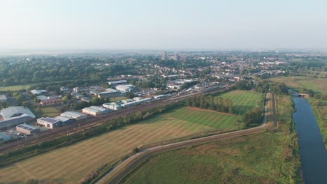 aerial view of a town with buildings, roads, and a river bordered by fields and trees. the clear sky and horizon enhance the urban landscape