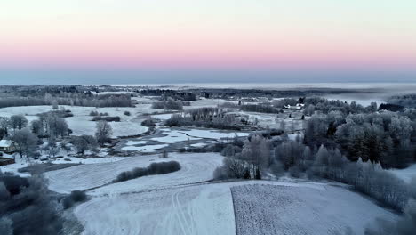 Stunning-snow-covered-countryside-with-trees,-fields-and-sunset