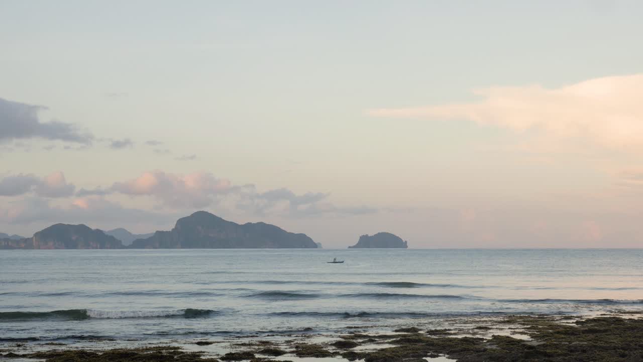 해질 무렵 석회암 절벽 앞에서 멀리 떨어진 보트에서 노를 젓는 남자의 슬로우 모션 샷