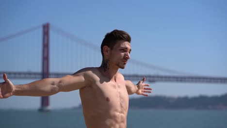 athletic shirtless man stretching arms at riverside