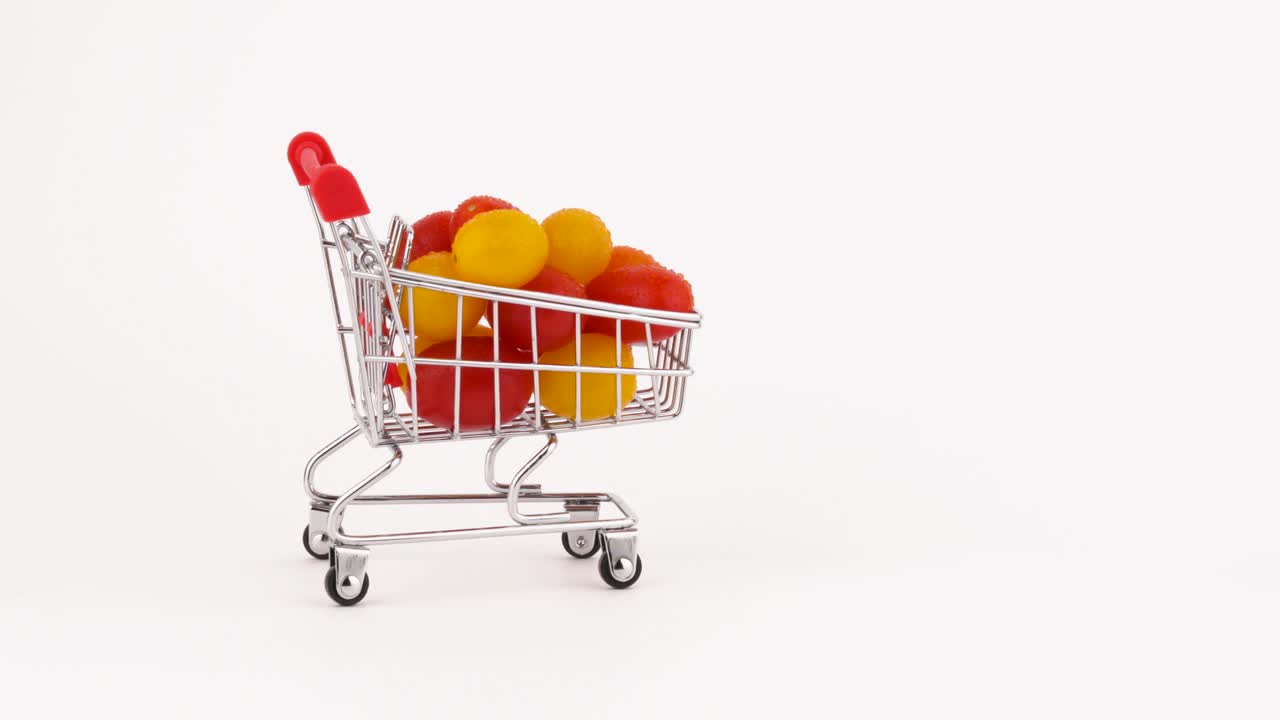 Carrello del supermercato in movimento pieno di un mucchio di pomodorini rossi e gialli con gocce d'acqua. Isolato su sfondo bianco. Primo piano. Macro