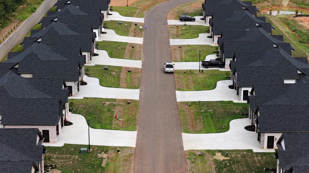 A white pickup rolls down the center of a new residential street framed by matching black roofed brick homes and pale driveways near Lynchburg, Virginia. Aerial forward wide shot