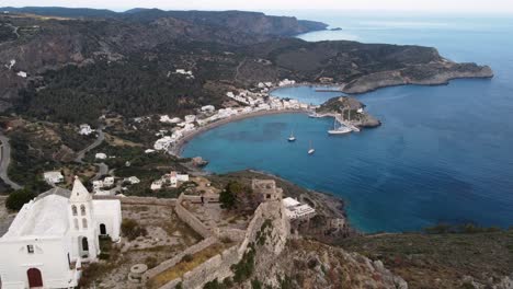 travelling aerial shot moving away from kapsali bay revealing chora castle church, greece