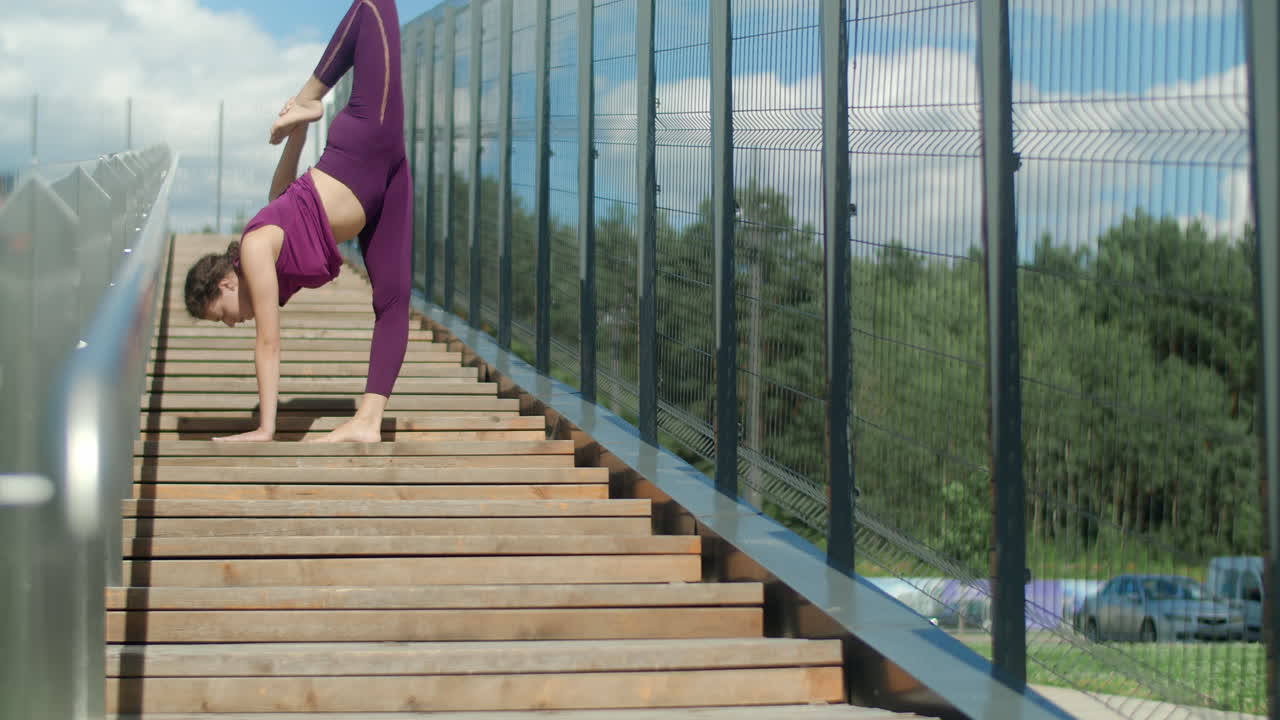 Woman performing a handstand leg split on outdoor stairs