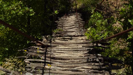 wooden hanging bridge with branches standing over wild river connecting people in mountains of albania