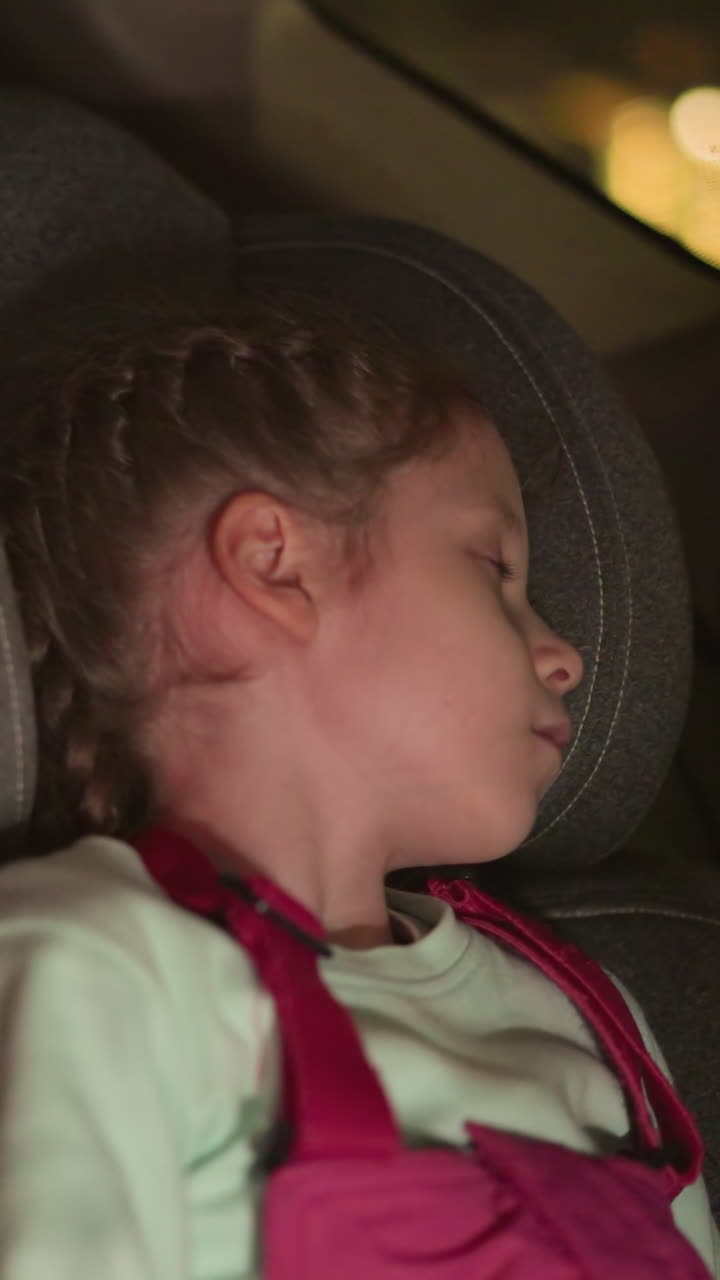 una vista cercana de un niño durmiendo pacíficamente en un asiento de coche, iluminado por el brillo suave de las luces ambientales, con coches de vista borrosa pasando por fuera