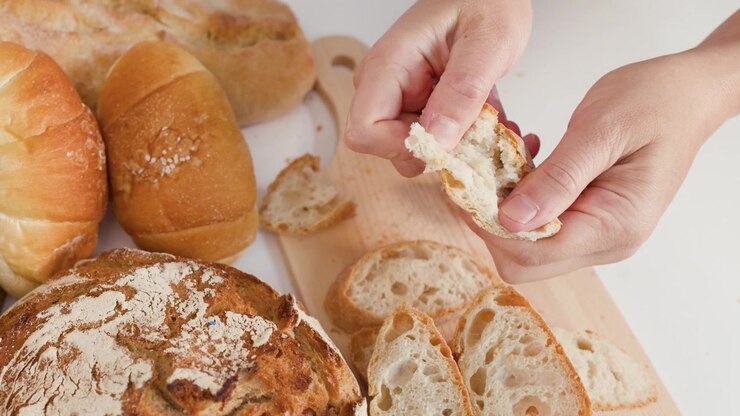 Close-up of hands tearing crusty bread over a wooden board with various artisanal loaves.