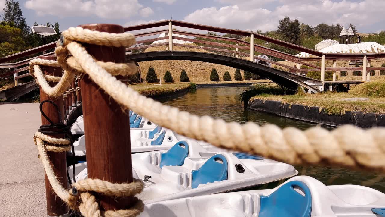 A serene view of white boats moored along a calm canal and a wooden bridge arching over the water at Volcanic Park in Orizaba city, Puebla, Mexico.
