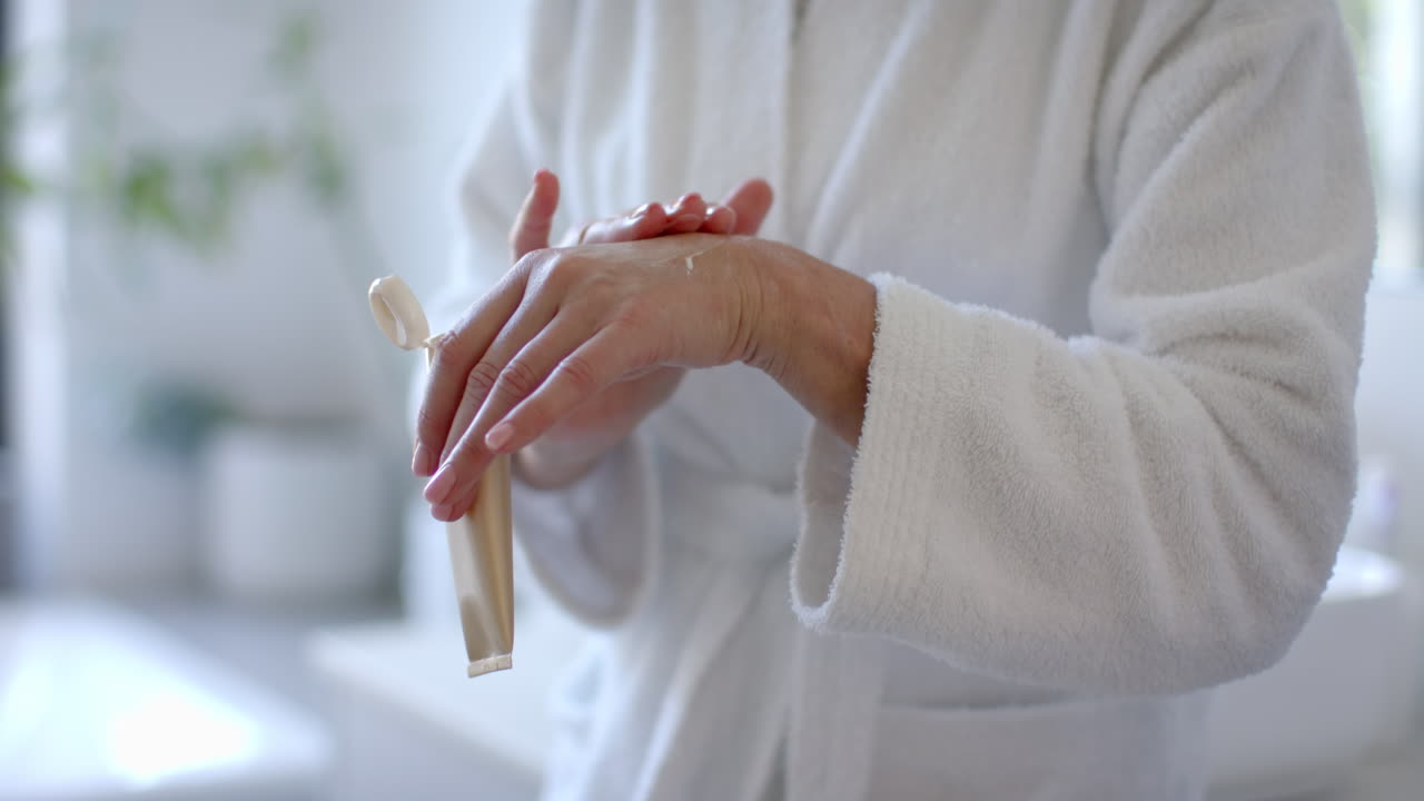 Applying hand cream, mature woman in bathrobe caring for skin at home