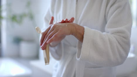 applying hand cream, mature woman in bathrobe caring for skin at home