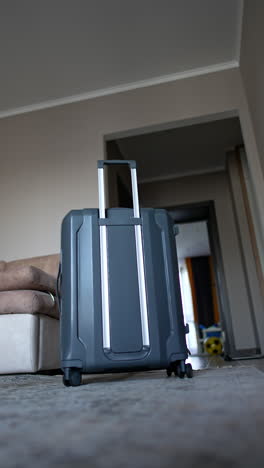 caucasian toddler enters the room with a big suitcase. kid pushes the suitcase and hides behind it. low angle view. vertical video.