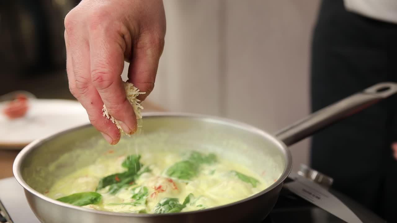 셰프 는 크리미 가 많은 스파나치 파스타 요리 에 치즈 를 첨가 하고 있다