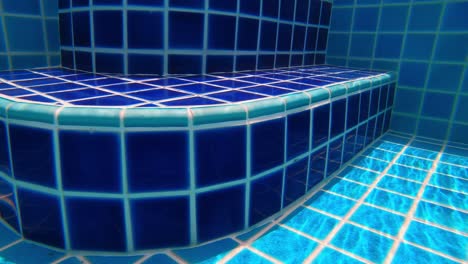 underwater footage of walking along the bottom of a swimming pool towards steps and exiting