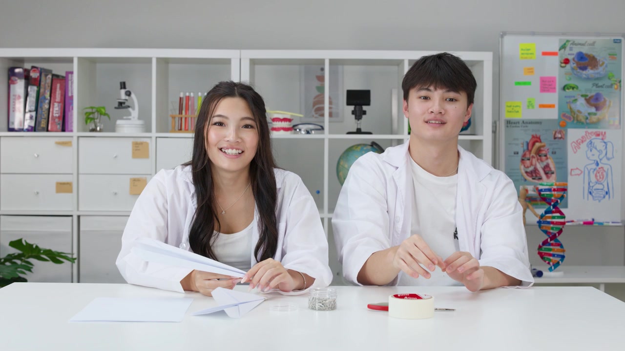 白い白衣を着た2人の学生が、理科の授業の実験中に紙飛行機の物理学をテストしている。