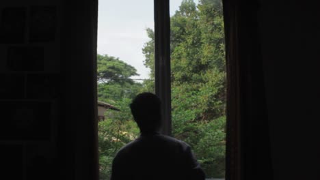 배경에 나무가 있는 창밖의 사진을 찍는 사진작가의 긴 실루엣