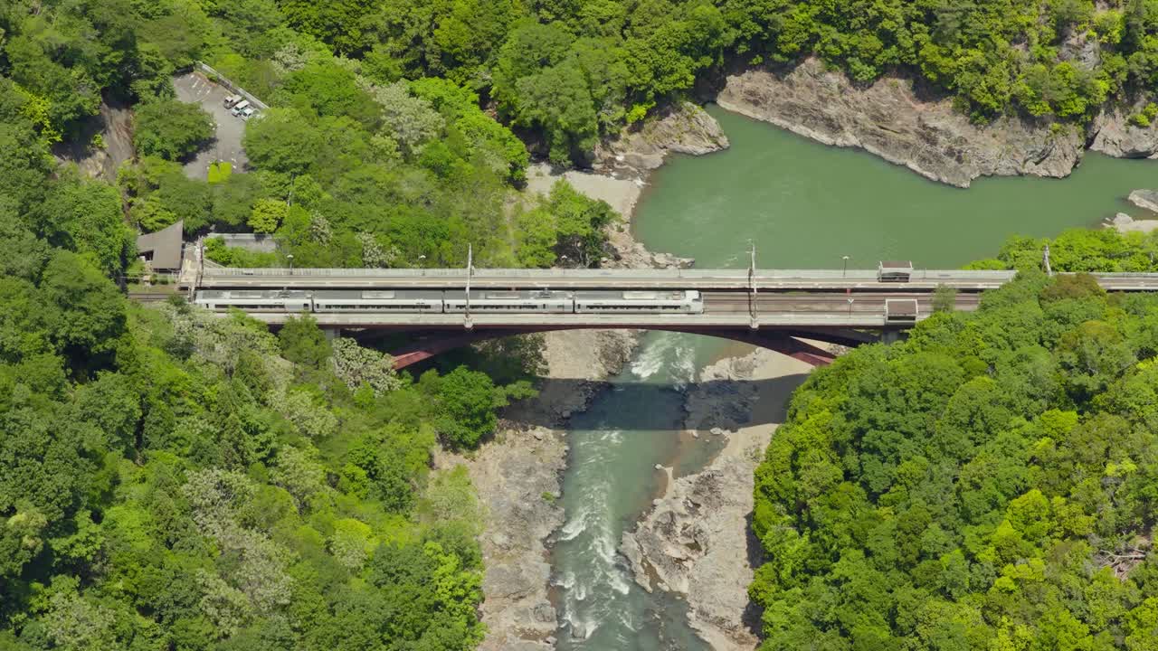 Aerial establishing fly bridge cross with Train riding at Arashiyama river landscape of Kyoto Japan, along lush Mountains