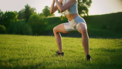 a young woman performs a static exercise on the grass for the leg and hip muscles. to rise on toes while sitting. exercise for the lower leg. training on the street in the park