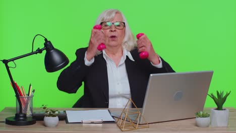 mujer de negocios senior haciendo ejercicio, bombeando los músculos de los brazos levantando pesas rosas, relajándose después del trabajo