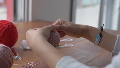 Woman-pulls-yarn-from-ball-as-she-continues-to-crotchet-small-pink-disc-for-hat