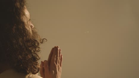 portrait of man with long hair and beard representing figure of jesus christ putting hands together in prayer