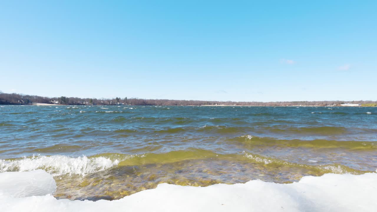 A peaceful winter scene at Lake Ronkonkoma, Long Island. Clear blue skies reflect over shimmering icy waters, creating a tranquil moment of natural beauty. Captures the serene charm of the season.