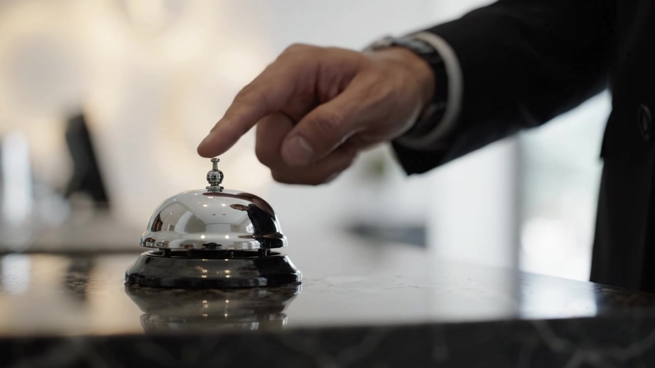 Un addetto professionale che interagisce con un campanello della reception in una moderna hall d'hotel, mostrando ospitalità ed eccellenza nel servizio clienti