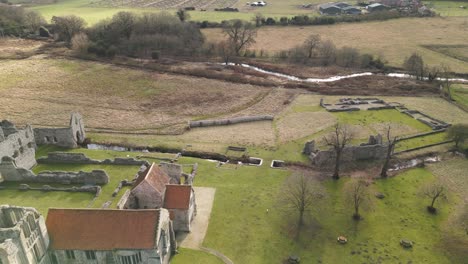 Castle-acre-priory-ruins-in-norfolk-with-surrounding-grassy-landscape,-shot-in-daylight,-aerial-view