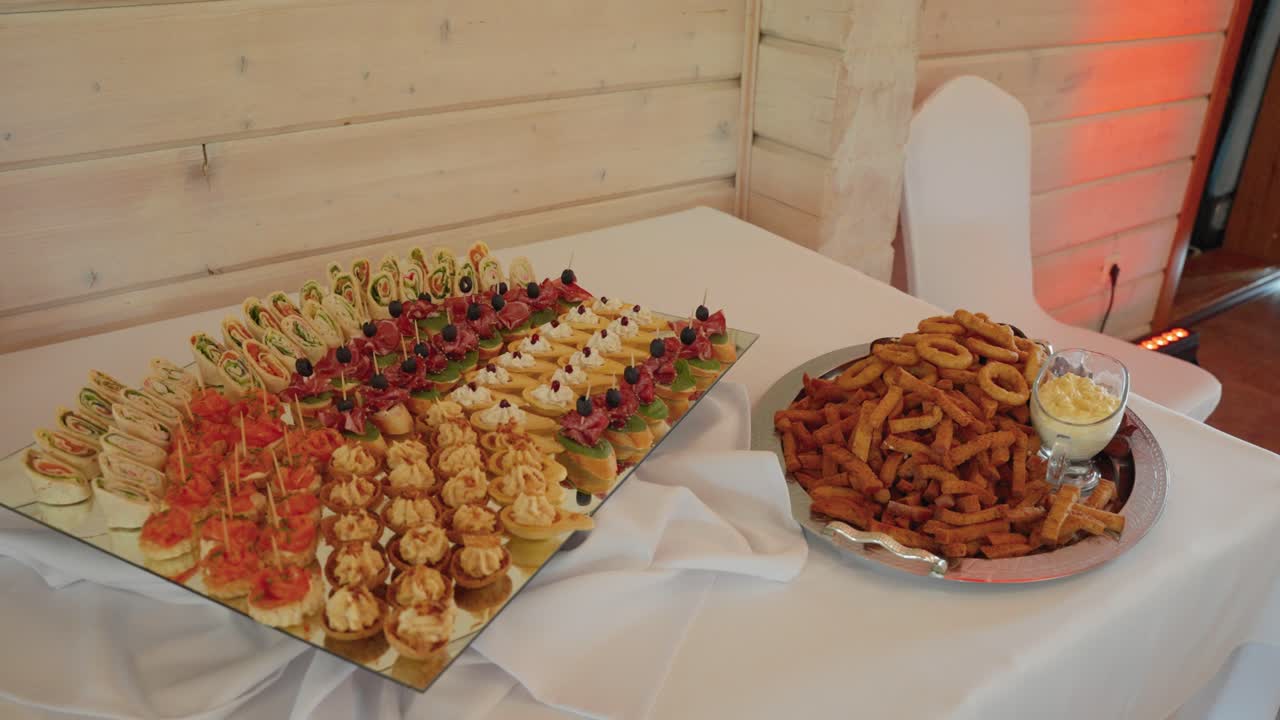 Un allestimento di catering splendidamente curato con una varietà di stuzzichini monoporzione su un impeccabile tavolo da buffet. La calda illuminazione interna valorizza l'atmosfera elegante e accogliente.