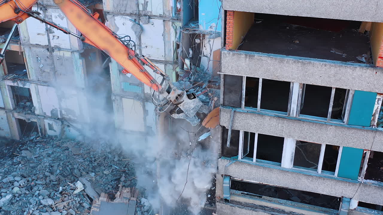 Demolition machine is breaking the floors into pieces and throwing them down. Powerful claw of excavator demolishing the ruined building.