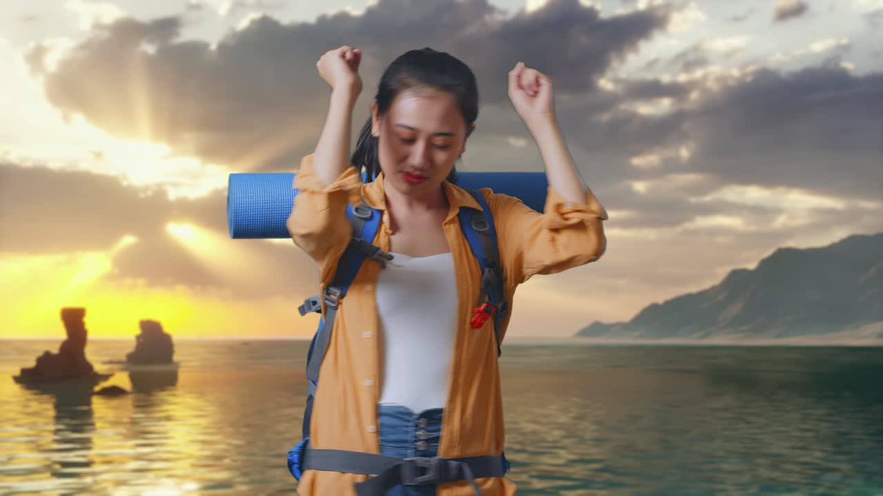 Escursionista asiatica con zaino da alpinismo che si diverte a ballare sulla spiaggia al tramonto
