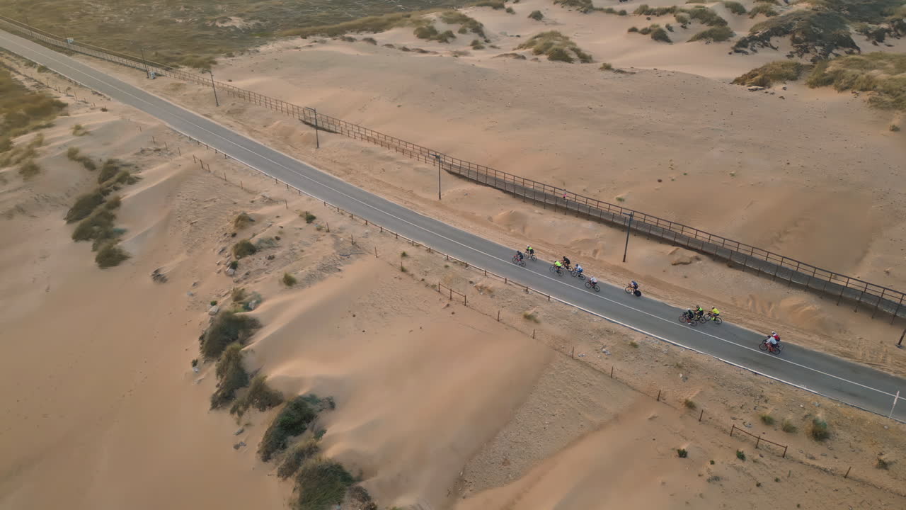 Aerial asphalt road running through sand desert. Group cyclists ride on highway