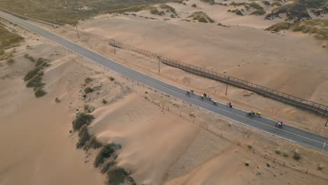 aerial asphalt road running through sand desert. group cyclists ride on highway