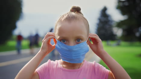 retrato de una hermosa chica mirando a la cámara con una máscara médica en un parque de la ciudad.