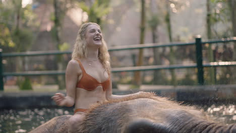 travel woman riding elephant in zoo playing in pool spraying water female tourist having fun on exotic vacation in tropical forest sanctuary