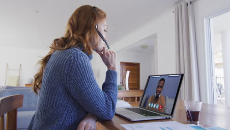 mujer caucásica usando portátil y auriculares de teléfono en videollamada con un colega masculino