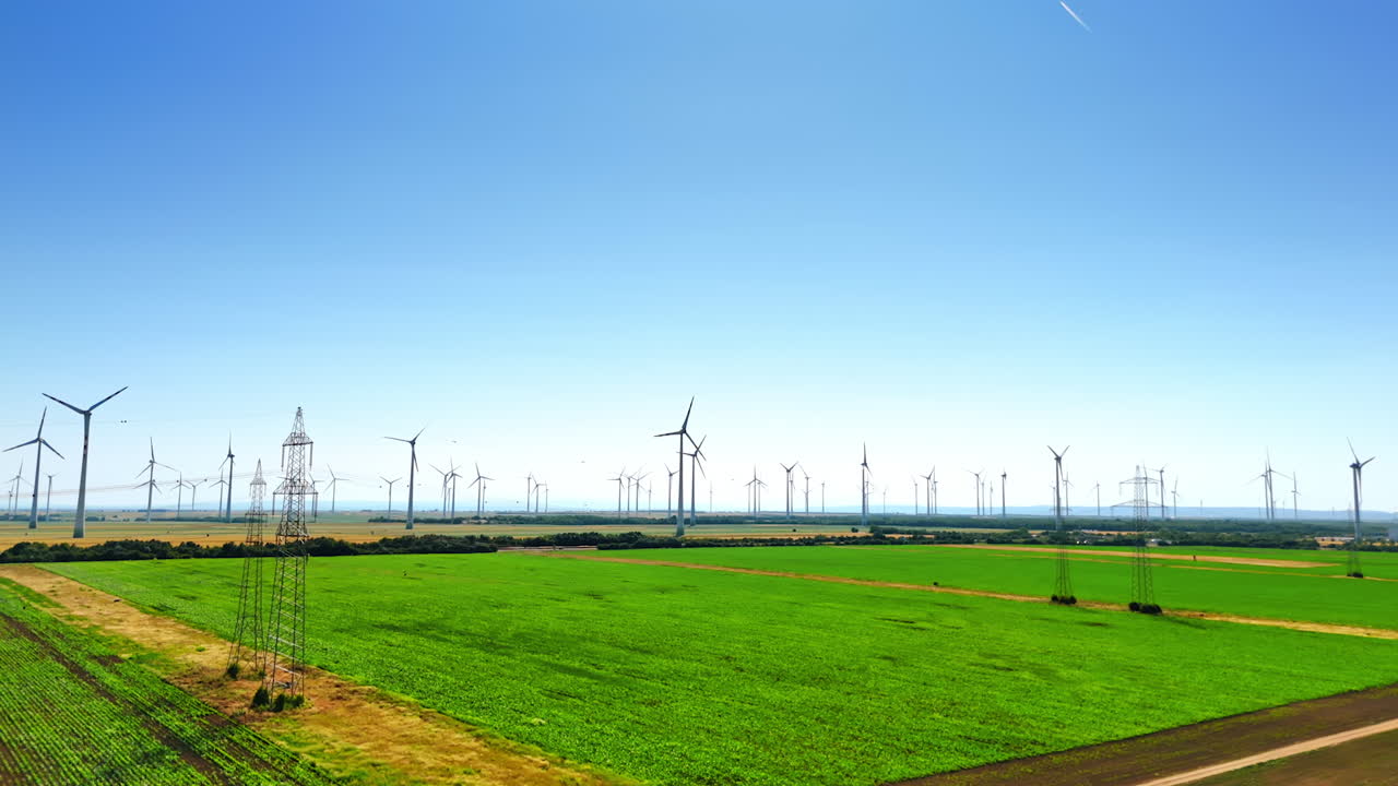 Turbines harness clean energy. Tall wind turbines stand in a green field under a clear blue sky, showcasing the shift to renewable energy