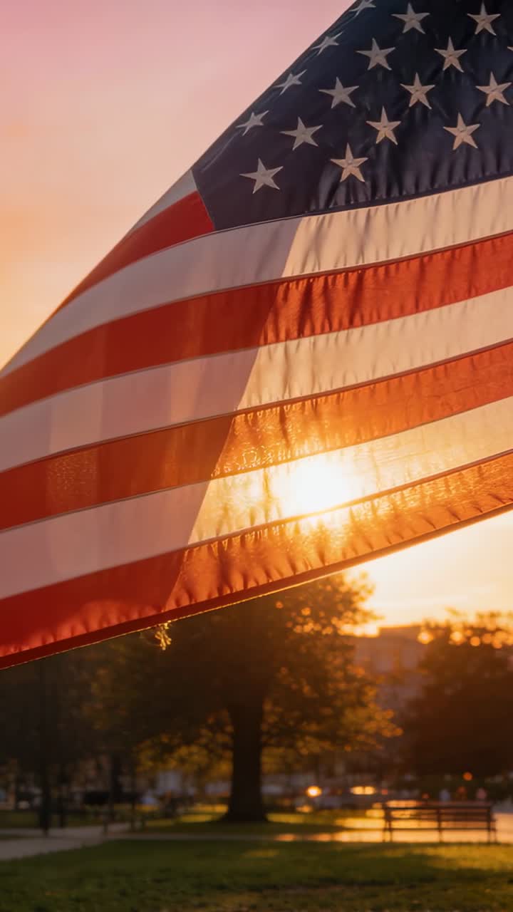 Bandiera americana che sventola, illuminata dal sole in controluce al parco, rivelando strisce rosse traslucide.
