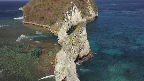 aerial view of atuh beach on nusa penida, indonesia on a sunny day and with crystal blue water hitting the rock formations