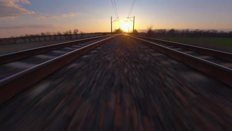 railway railroad aerial drone shot, fpv shot with hyperlapse like movement, flying towards a sunset horizon with fast speed on the tracks