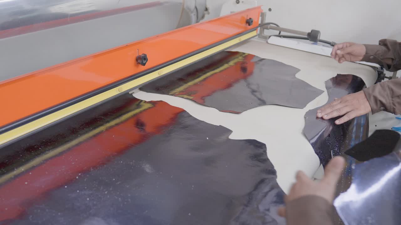 Close Up Shot Of Leather Hides Being Placed Onto A Industrial Foiling Machine In A Factory By Two Workers