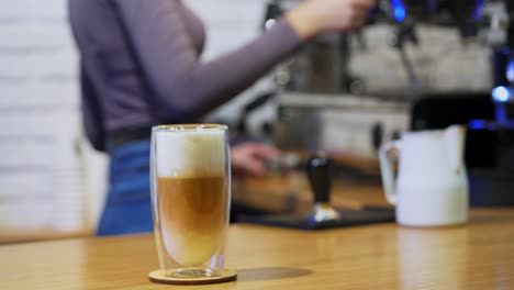 cappuccino or latte in glass. woman puts drink from coffee machine. fresh coffee with whipped cream in tall clear glass on table. close-up.