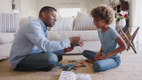 Pre-teen-girl-and-grandad-sitting-on-the-floor-in-living-room-constructing-a-model-robot,-side-view