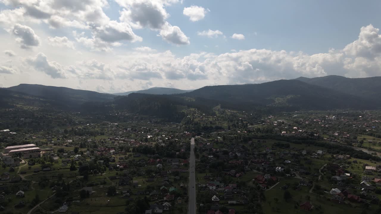 volando sobre la calle principal en un pequeño pueblo rodeado de colinas cubiertas de bosque en un día soleado y cálido