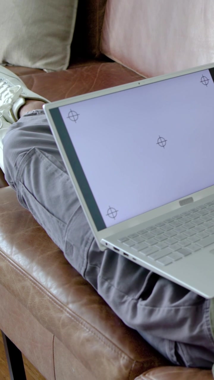 Video verticale: Uomo sdraiato in top verde che muove la mano su un pad, inclina il laptop sul divano e controlla un modello