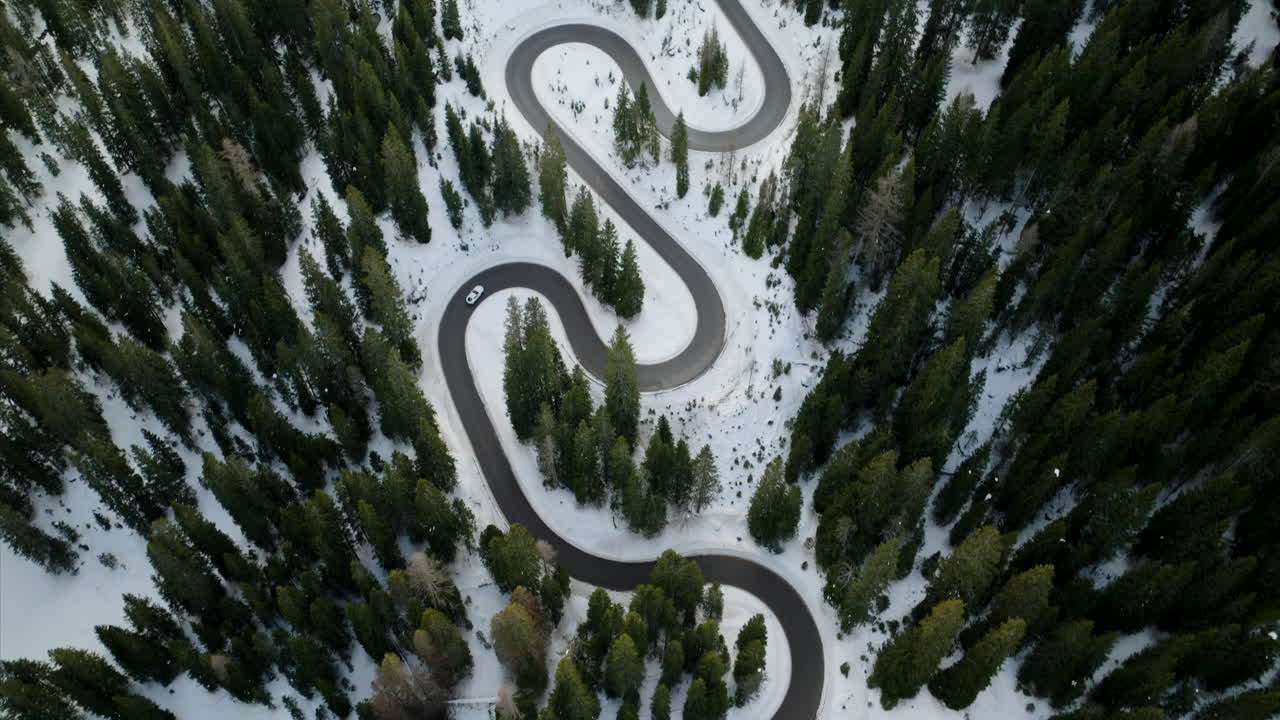 vista aérea de un coche conduciendo a través de la nieve cubierta giau pasar a través del bosque alpino