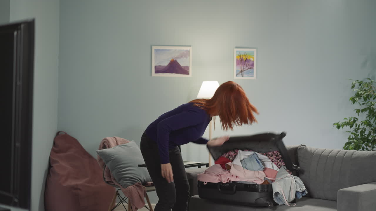 Irritated woman throws clothes heap into suitcase on sofa