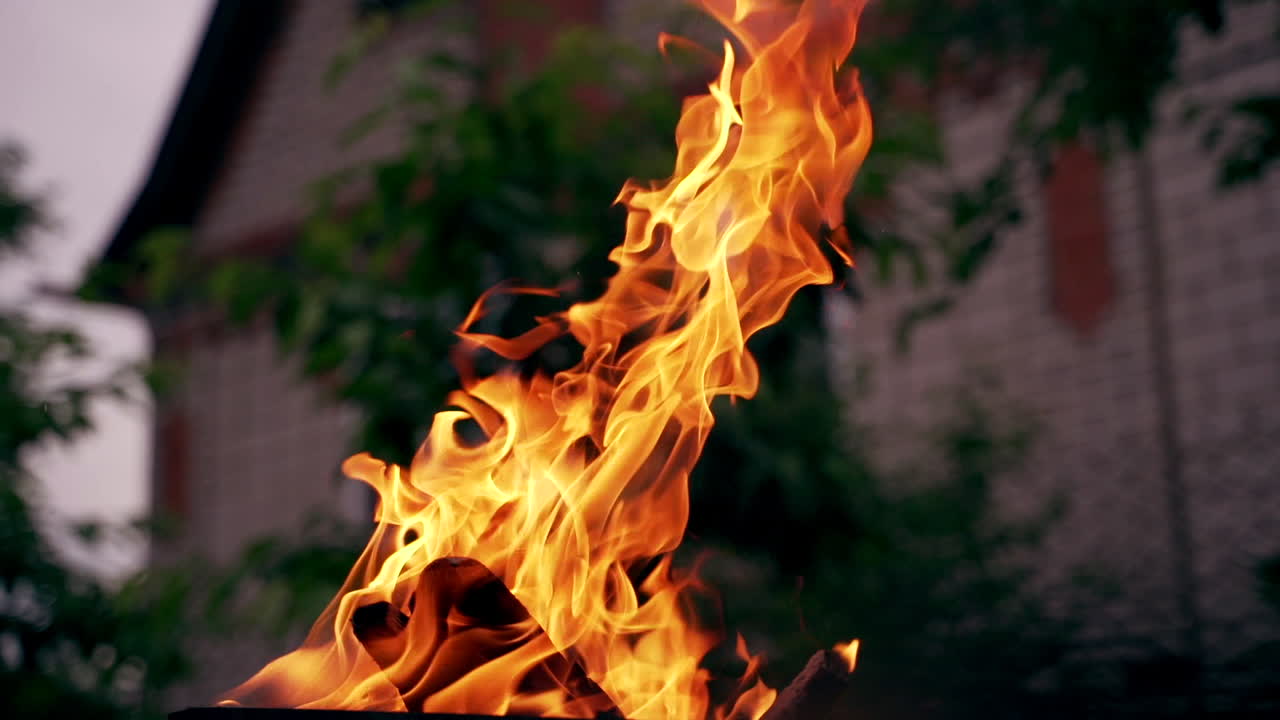 Excellent view on wood burning with orange fire flame outdoors. Natural texture of bright fire on blur building background in the evening.