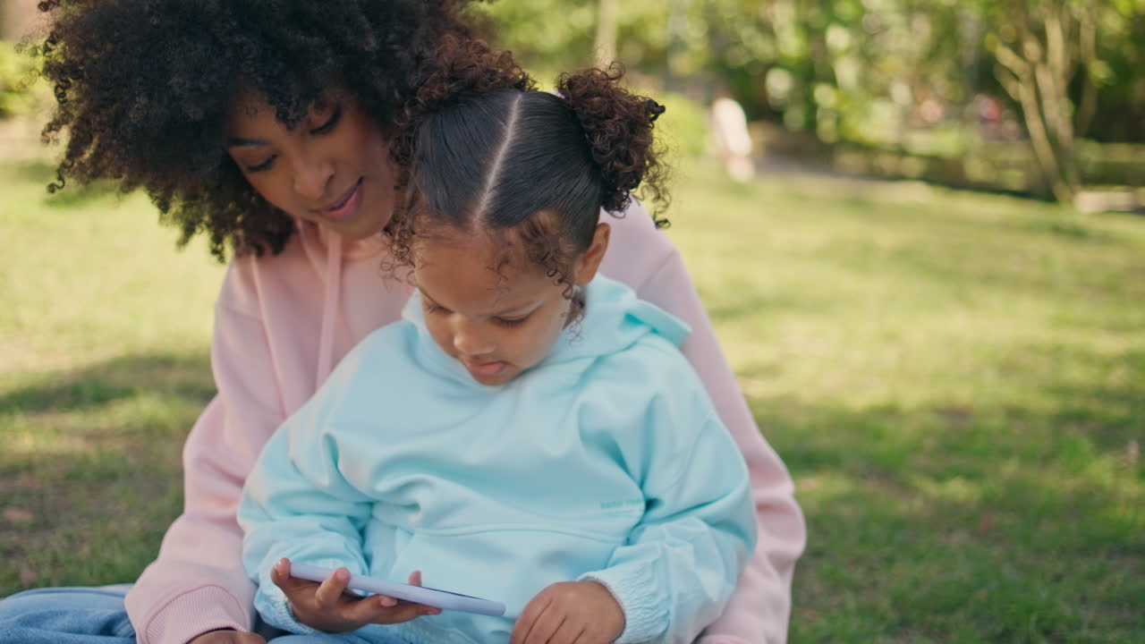 feliz amily buscando teléfono en la naturaleza de cerca. mujer mostrando juegos a la chica