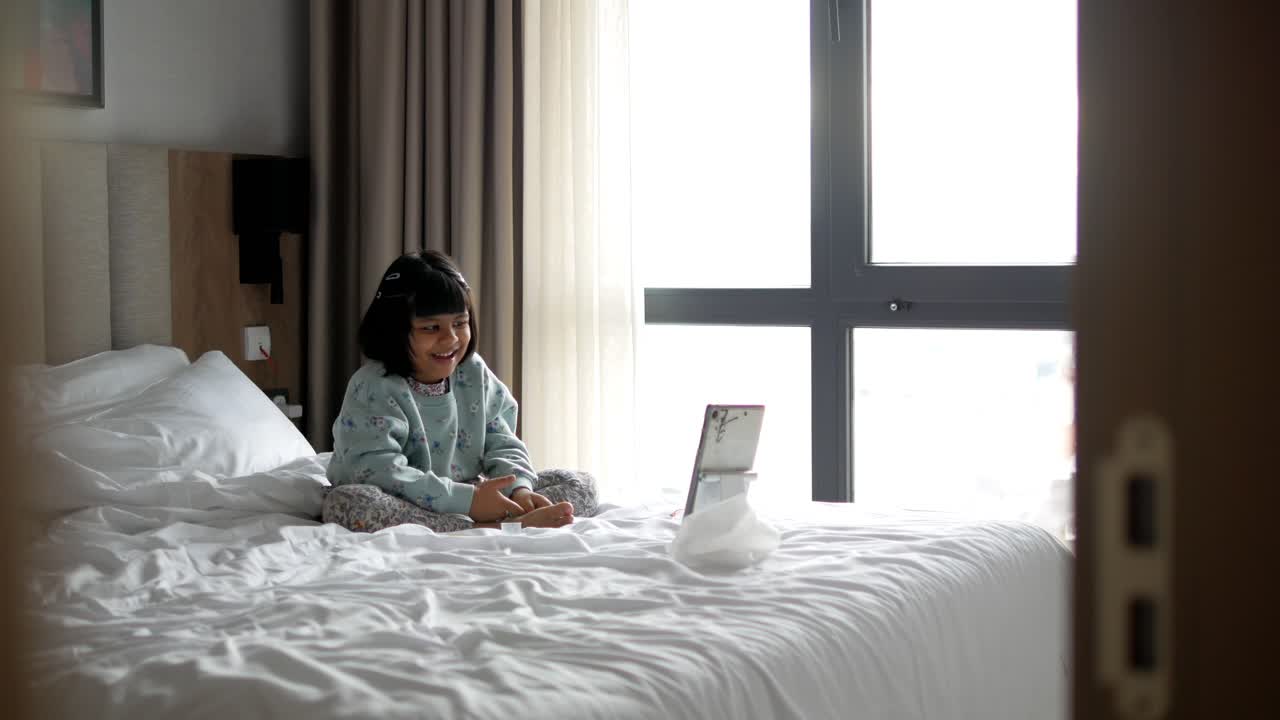 작은 소녀가 호텔 방에서 태블릿에서 비디오를 보고 있습니다.